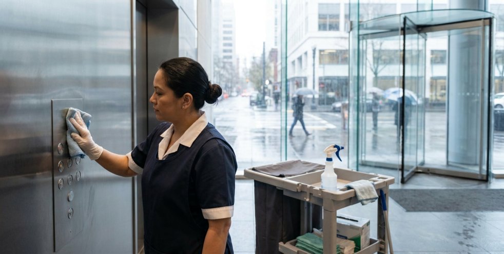 Facility cleaner disinfecting elevator buttons in a rainy Portland office lobby near the entrance